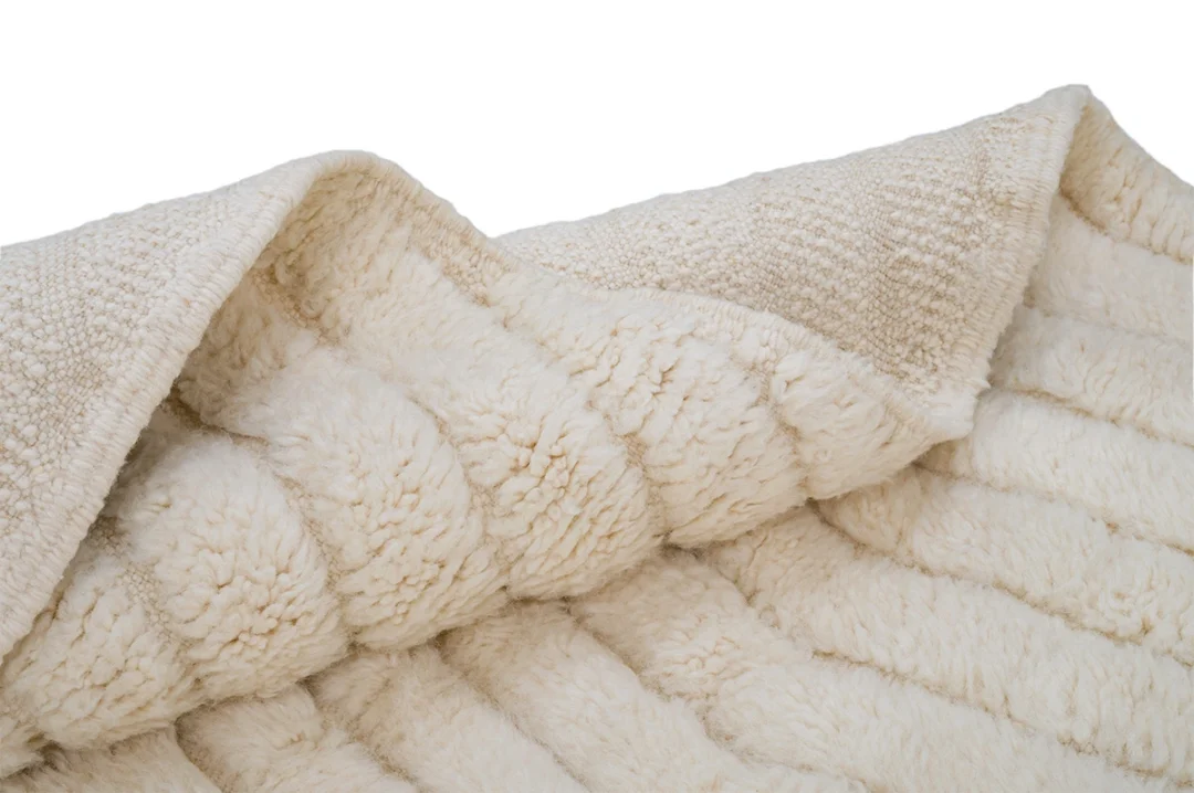 A close-up view of a cream-colored, textured fleece blanket with a soft, plush surface and a slightly folded edge.