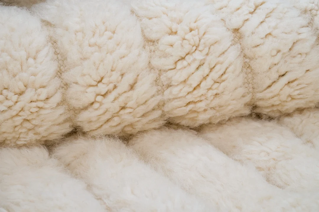 Close-up view of a textured, cream-colored wool or fleece fabric, showing soft, fluffy fibers in a quilted pattern.