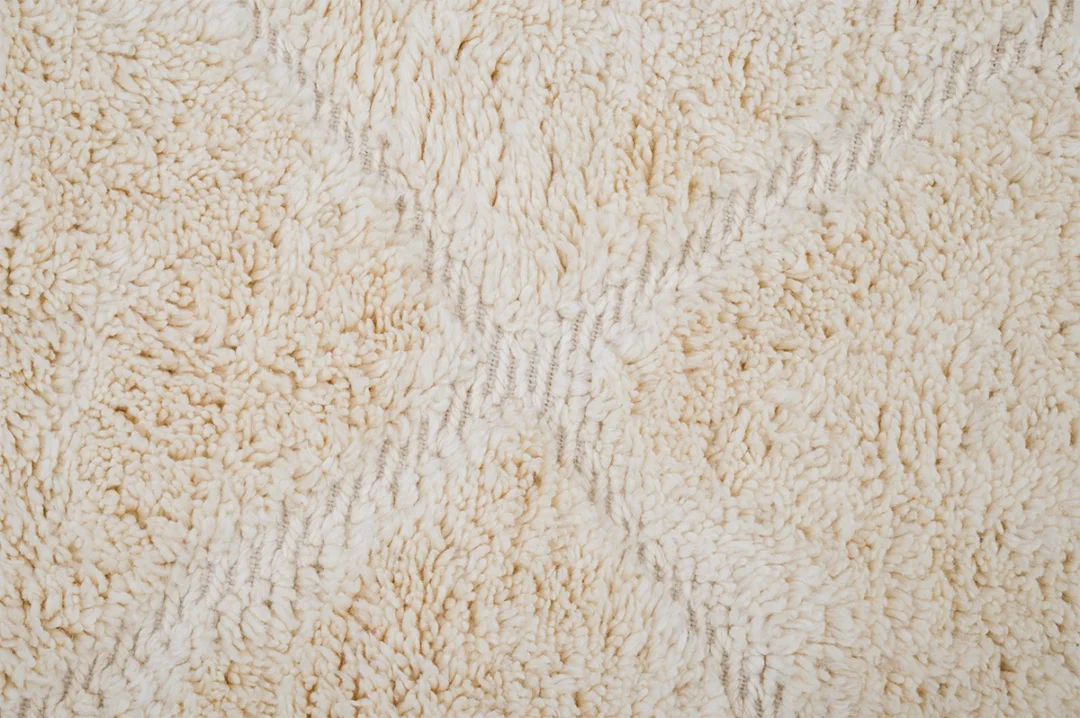 Close-up of a cream-colored, textured, shaggy carpet with subtle intersecting grey lines forming a simple pattern.