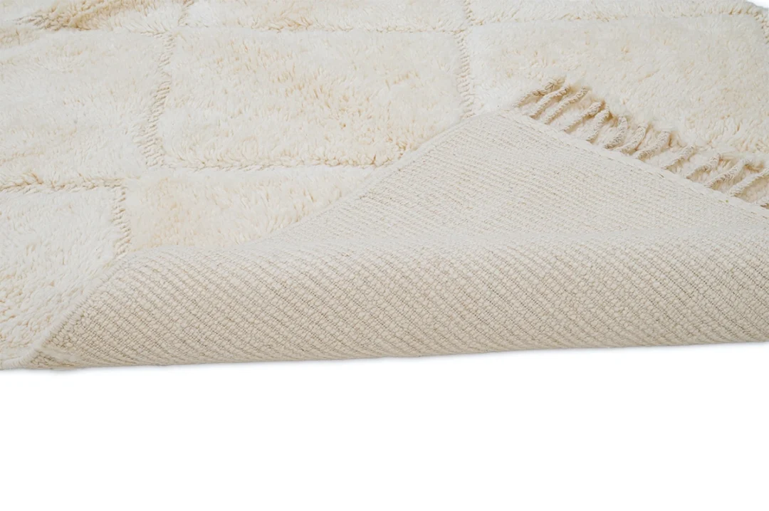 A cream-colored textured rug is shown with one corner folded over, revealing the woven underside.