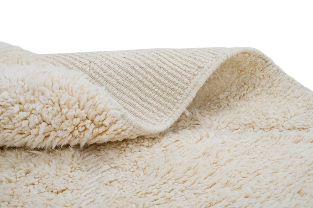 A close-up of a cream-colored, textured, fluffy rug with a visible woven underside.