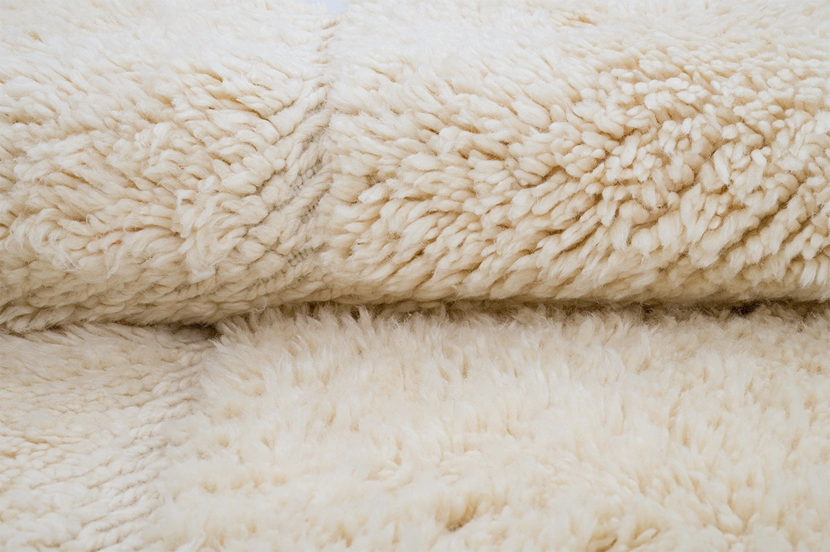Close-up view of soft, fluffy cream-colored fleece fabric with a textured, woolly surface.