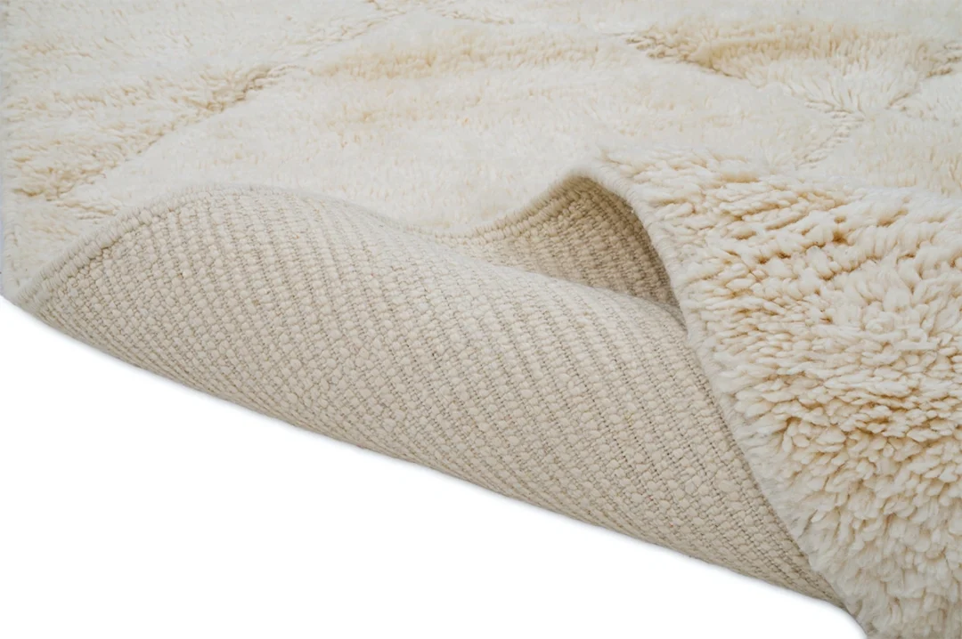 A close-up of a cream-colored, textured rug with one corner folded to show the woven underside.