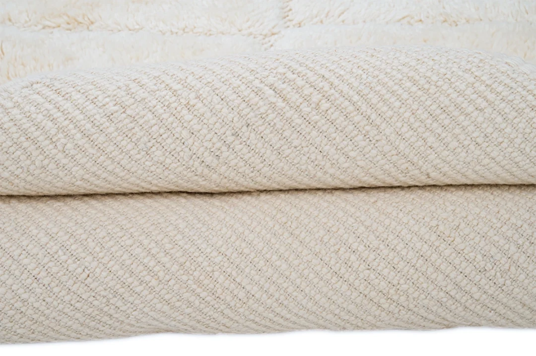 A close-up view of a folded, textured cream-colored blanket with a woven pattern.