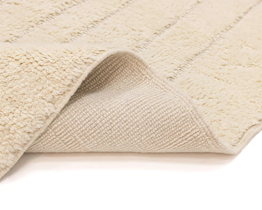 A close-up of a beige, textured, rectangular rug with one corner flipped over showing the woven underside.