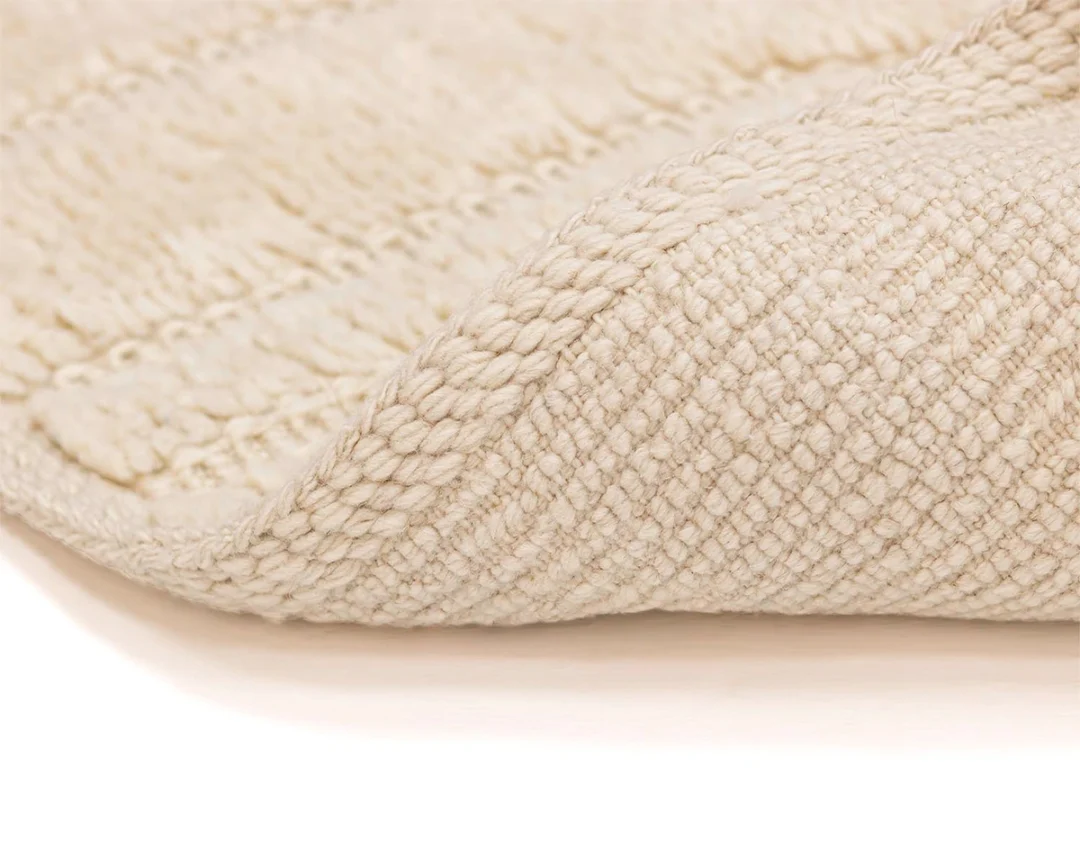 Close-up of a cream-colored woven fabric with a textured, braided edge, partially folded over on a flat surface.