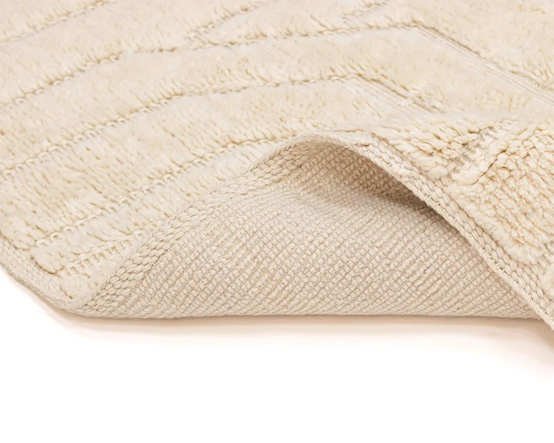 Close-up of a cream-colored textured rug with one corner slightly lifted to show the woven underside.
