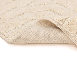 Close-up of a cream-colored textured rug with one corner slightly lifted to show the woven underside.