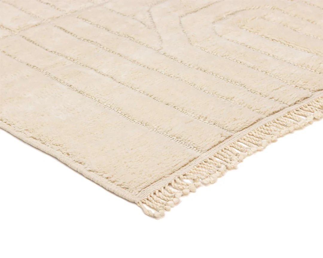 Close-up of a cream-colored textured rug with a subtle geometric pattern and fringed edges.