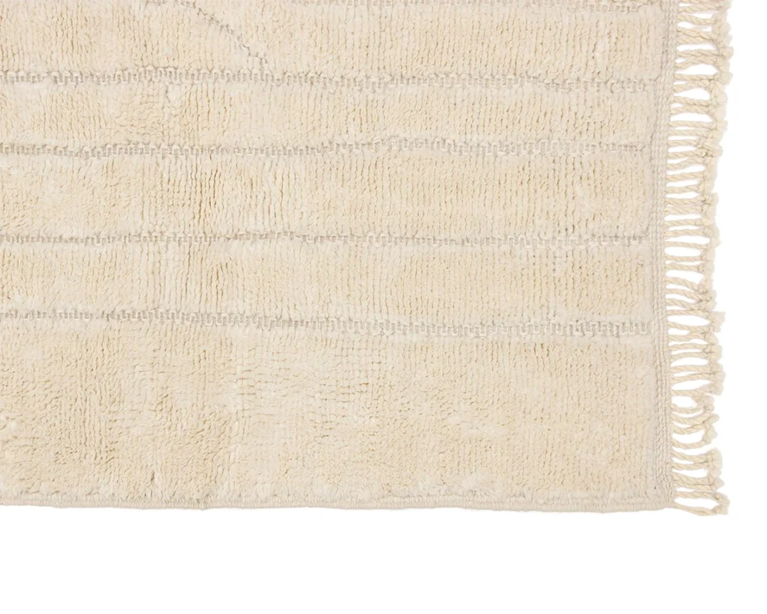 Close-up of a beige textured rug with horizontal lines and fringed tassels along the right edge.