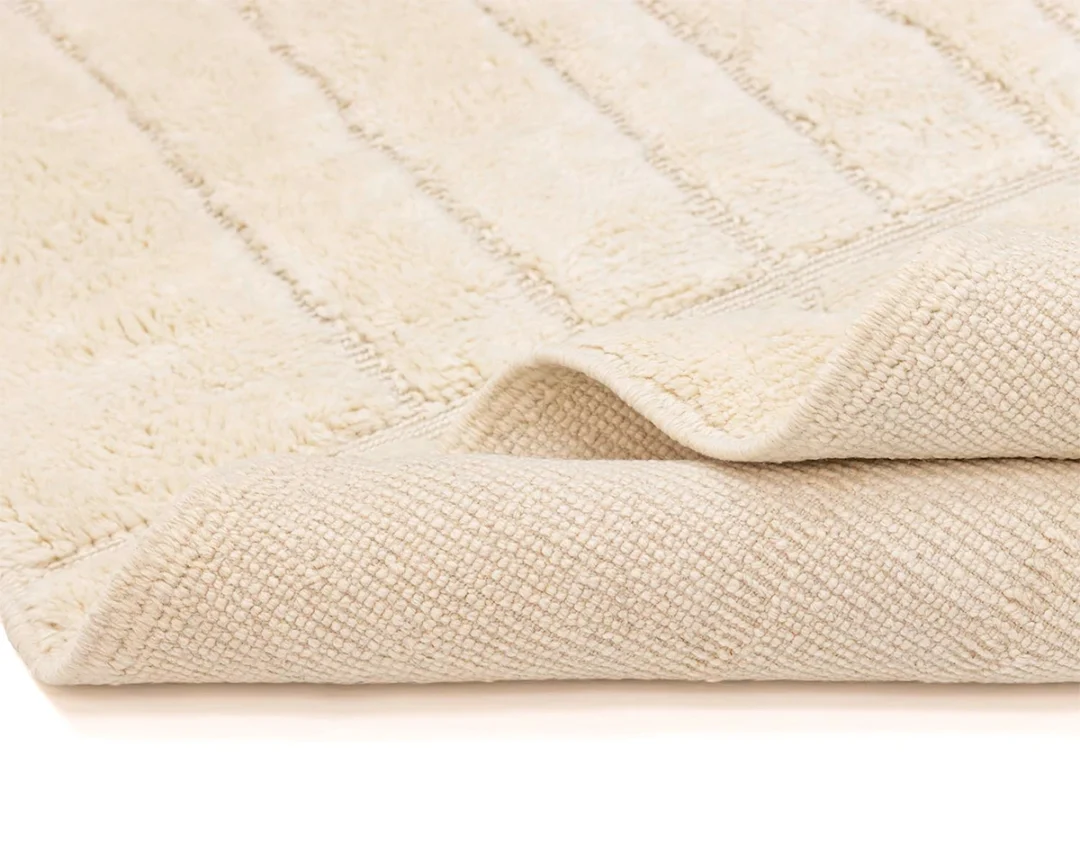 A close-up view of a folded beige bath mat with a textured pattern and soft, absorbent surface.