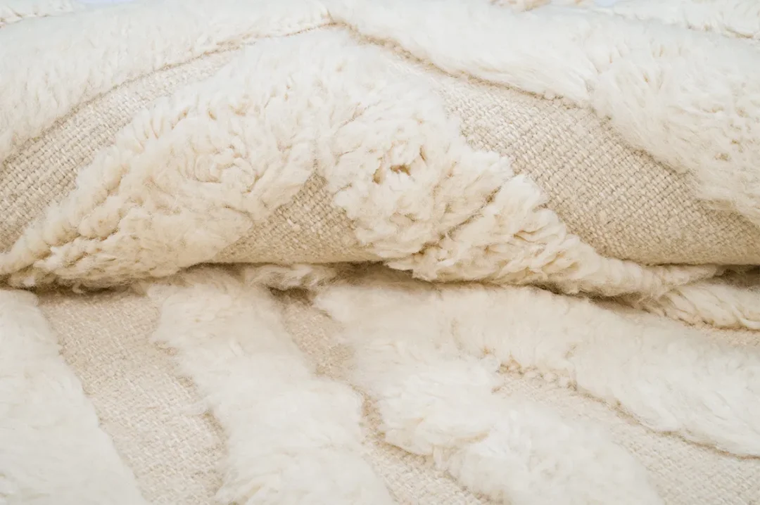 Close-up of a cream-colored, textured, fluffy rug with diagonal patterns and soft, plush fibers.