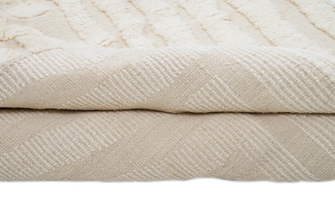 A folded beige textured rug with a woven diamond pattern and soft, plush surface visible on top.