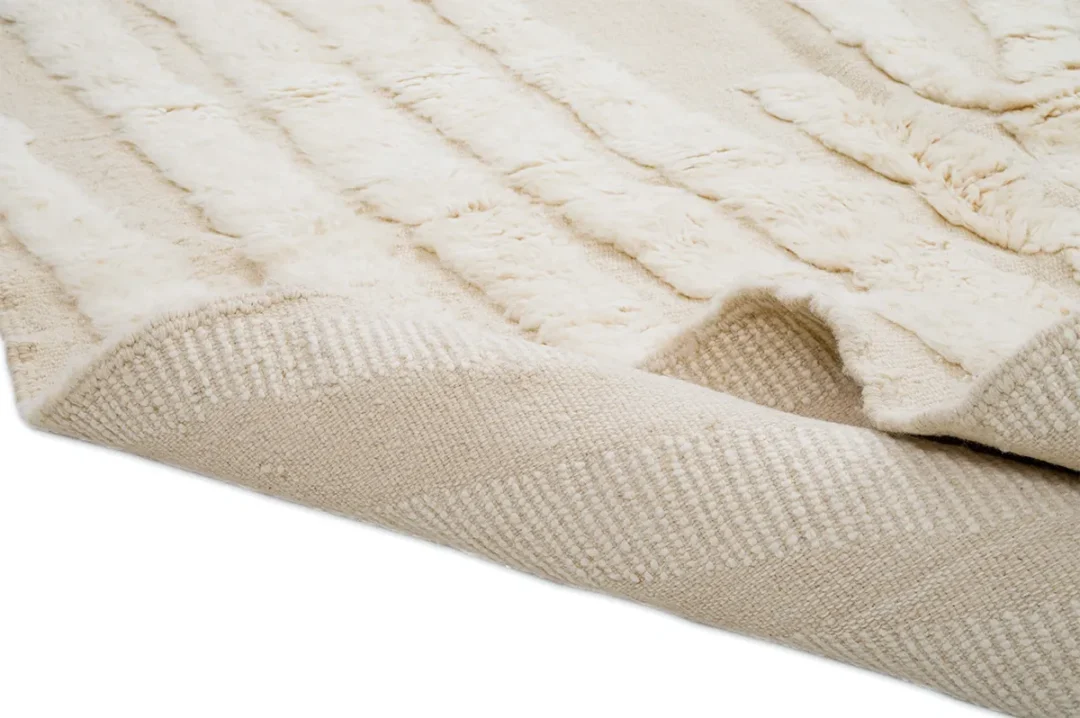 Close-up of a beige textured area rug with a raised, soft pattern and slightly curled corner on a white background.