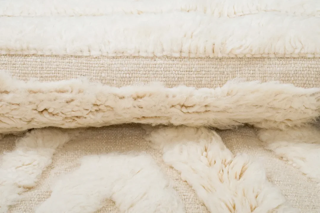 Close-up of a folded, cream-colored textured rug with a mix of flat and shaggy woven patterns.