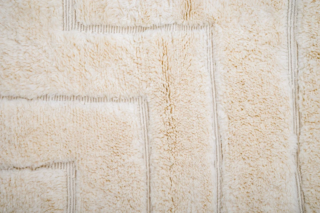 Close-up of a textured, cream-colored, rectangular-patterned shaggy rug with visible soft fibers and seams.