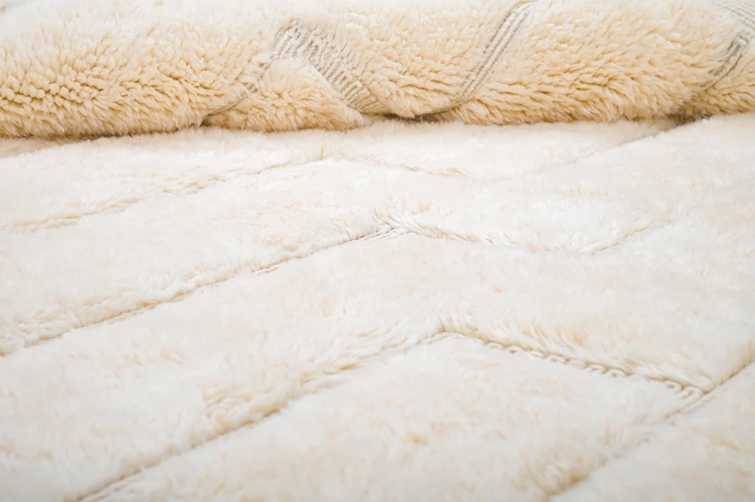 Close-up view of a soft, cream-colored, textured blanket or fabric with a plush, fuzzy surface and subtle zigzag patterns.