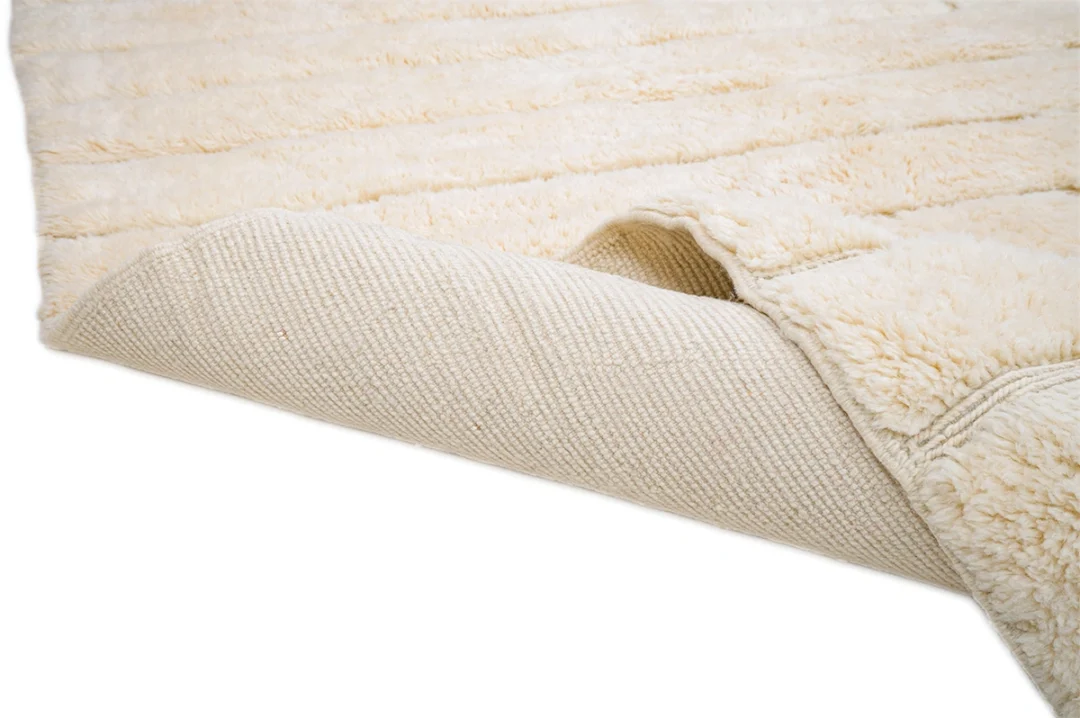 A close-up of a cream-colored, textured rug with a corner flipped over, revealing the woven backing.
