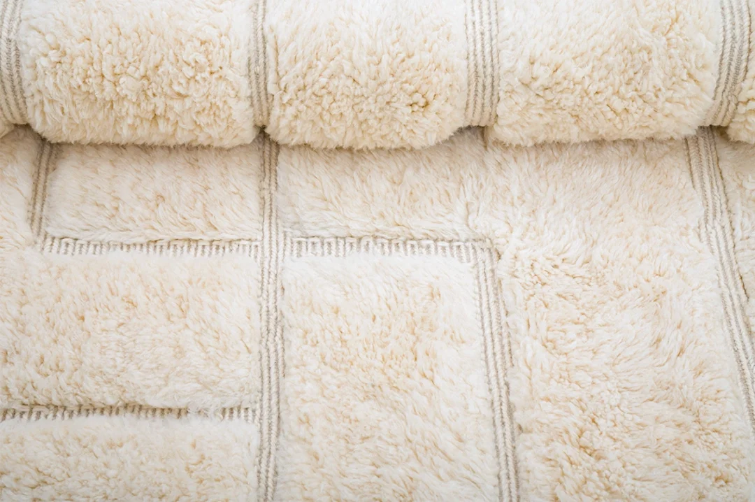Close-up of a rolled, fluffy cream-colored rug with a square pattern and textured surface.
