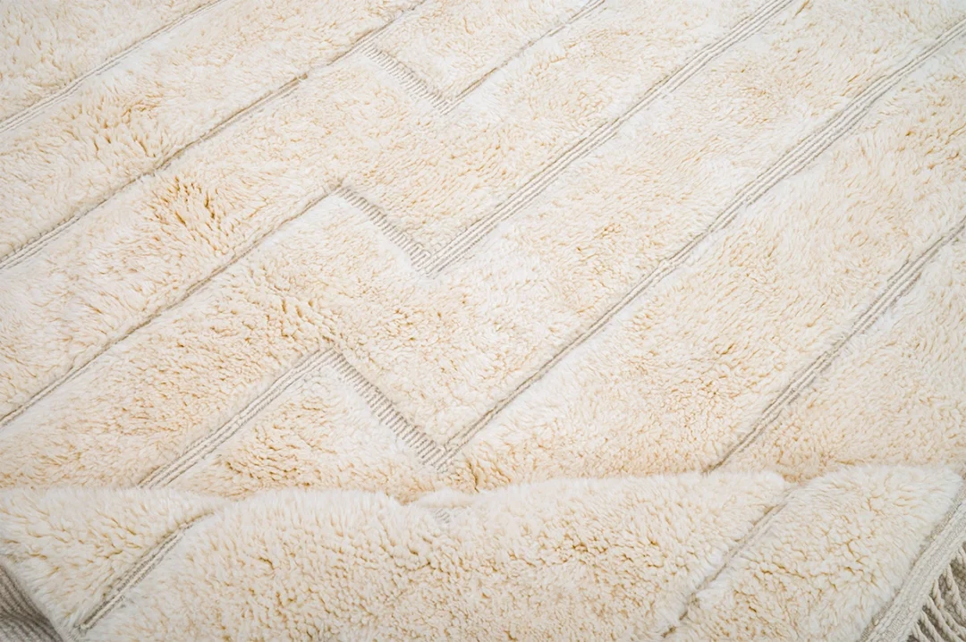 A close-up of a beige, textured fabric with a geometric zigzag pattern and soft, fluffy surface.