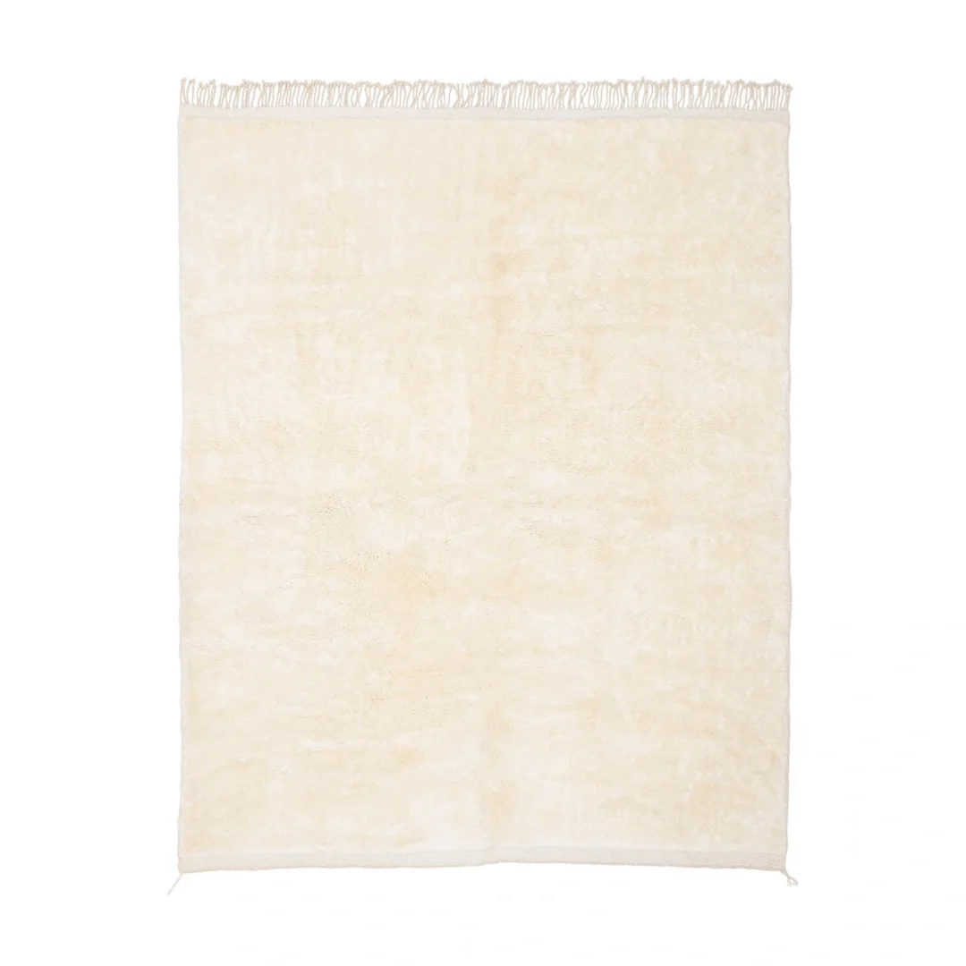 A rectangular, cream-colored rug with short fringe along the top edge, displayed on a white background.