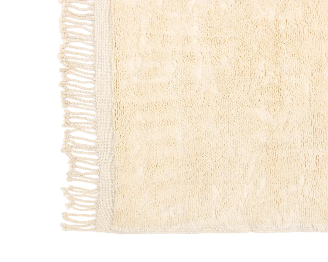 A close-up of a beige textured rug with fringe along the edge, showing a soft and woven fabric pattern.