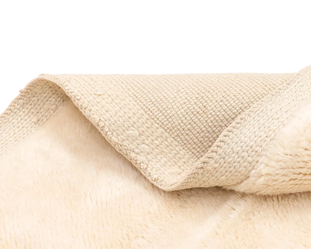Close-up of the corner of a beige, textured rug showing both its soft, plush top and woven underside.