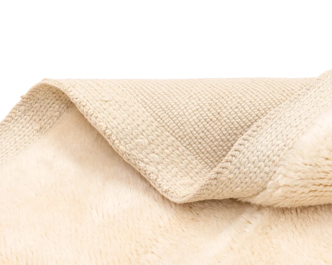 Close-up of the corner of a beige, textured rug showing both its soft, plush top and woven underside.