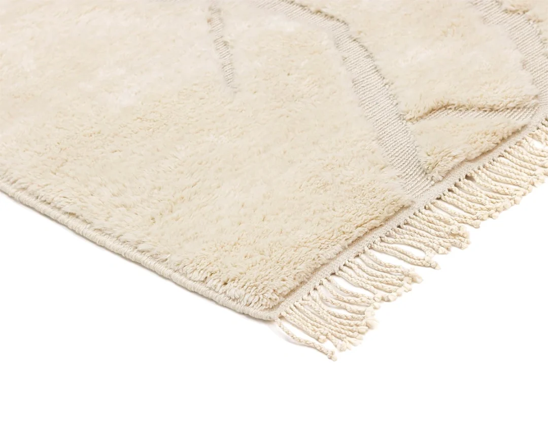 Close-up of a cream-colored, textured rug with fringed edges, photographed against a white background.