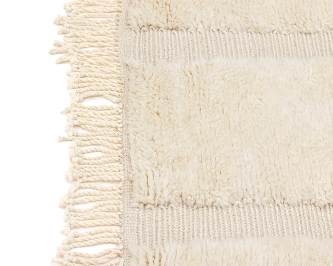 Close-up of a cream-colored textured rug with thick horizontal stripes and fringed edges on the left side.