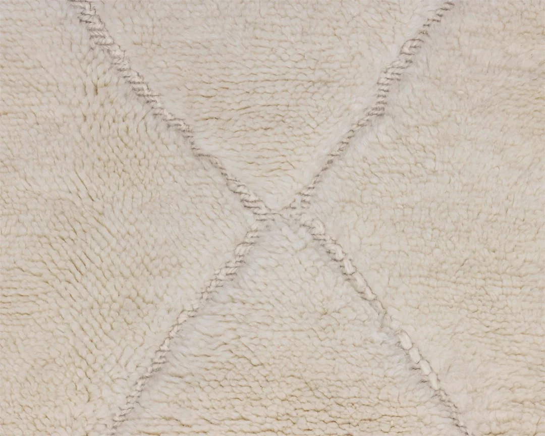 Close-up of a cream-colored, textured wool rug with a subtle diamond pattern formed by slightly raised lines.