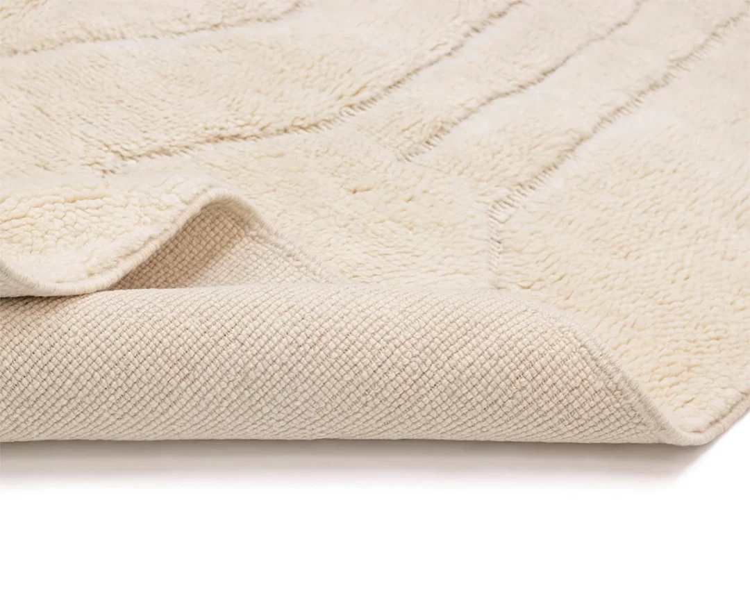 Close-up of a cream-colored textured rug, partially folded to show both the soft tufted top and the woven underside.