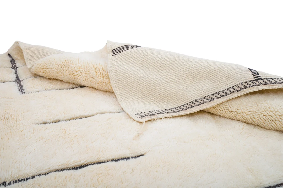 A cream-colored, plush area rug with a simple linear pattern is partially folded to show its thick texture and woven underside.