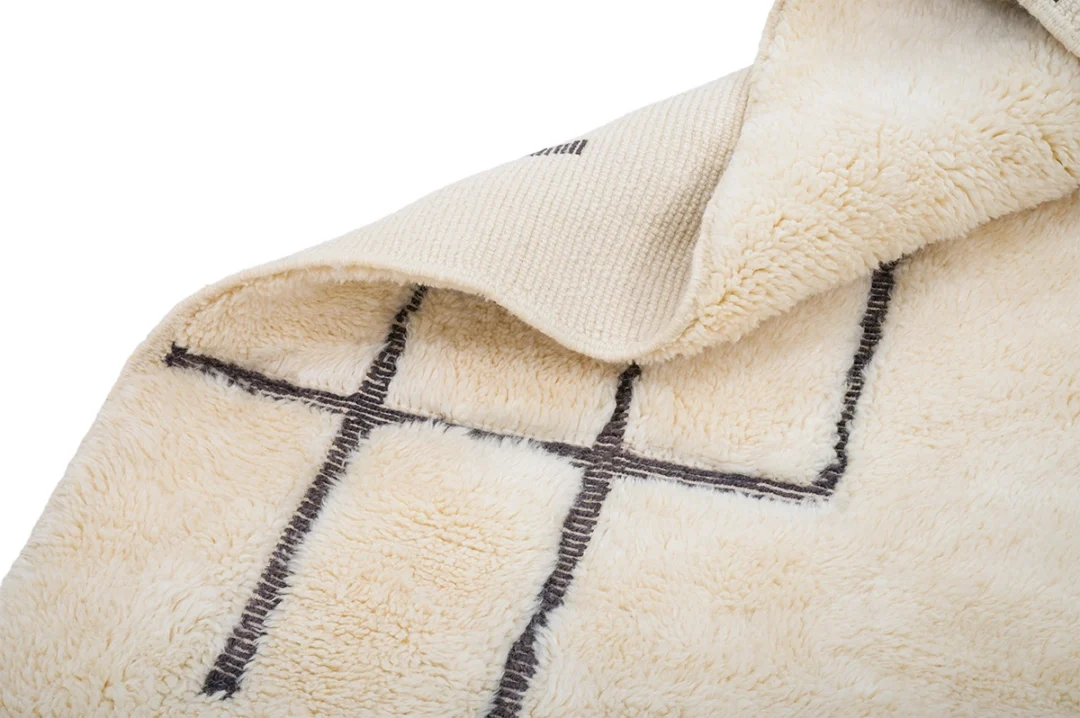 A cream-colored, fluffy rug partially folded over, displaying a grid pattern with black lines on its surface.
