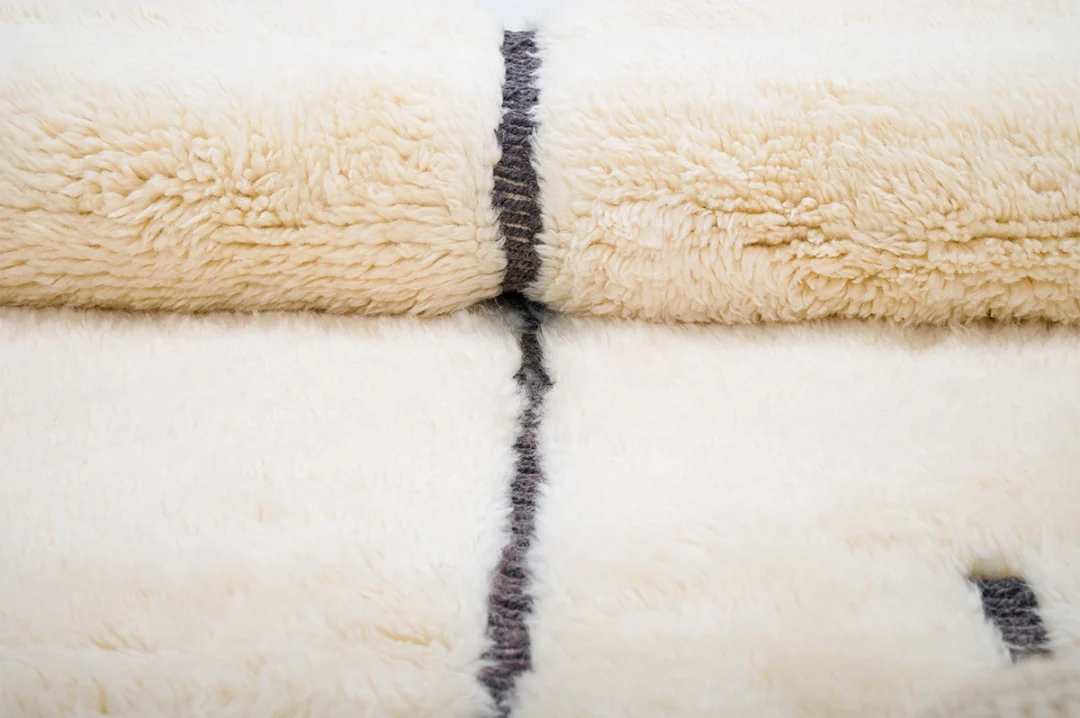 Close-up of a folded, cream-colored, fluffy blanket with a single dark stripe running through the center.