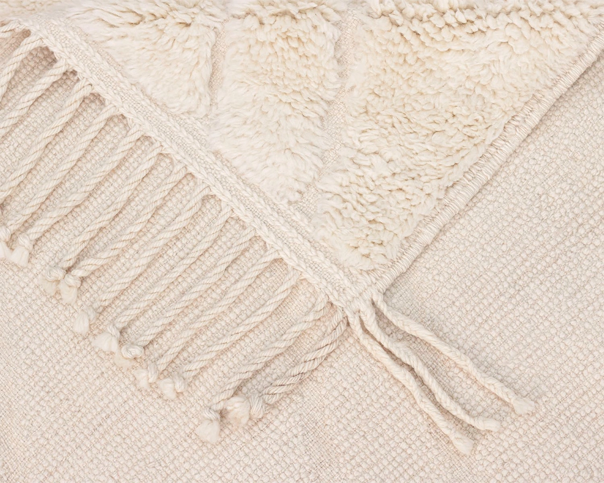 Close-up of a cream-colored woven textile with a textured, fluffy section and a row of twisted fringe tassels along the edge.
