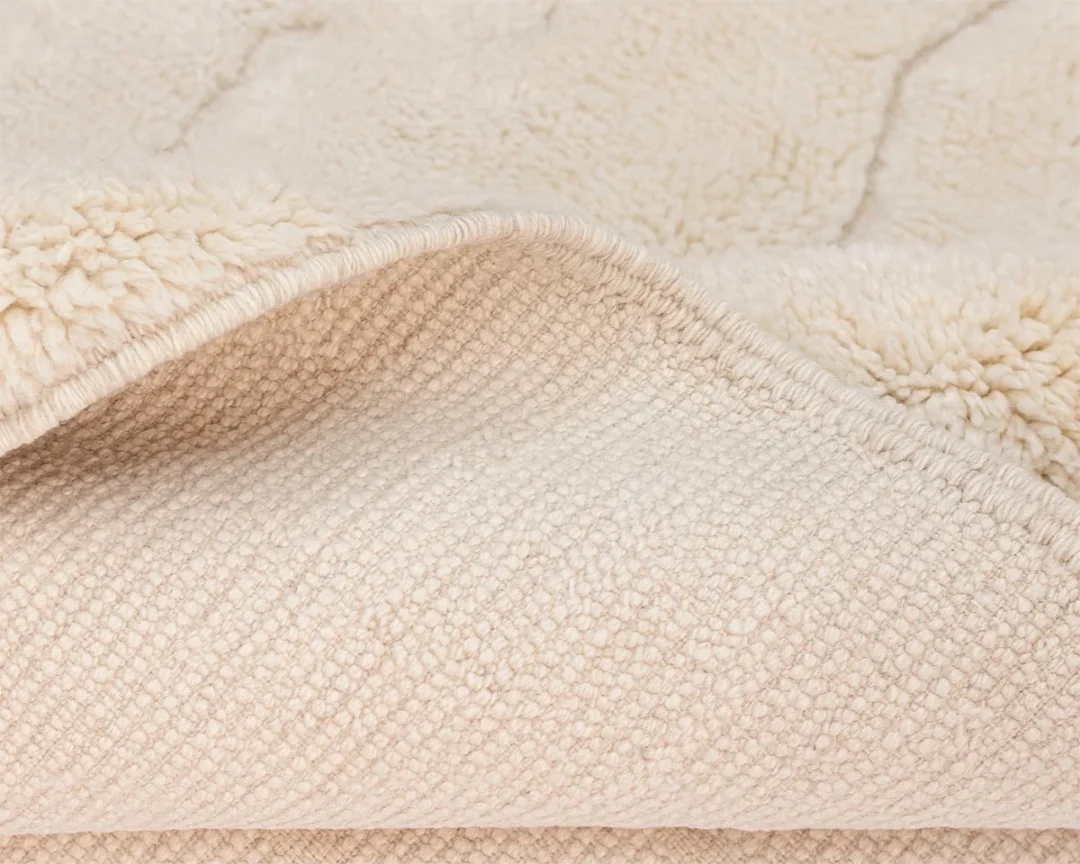 Close-up of a beige textured rug, showing a folded edge to reveal both the soft, shaggy surface and the woven underside.