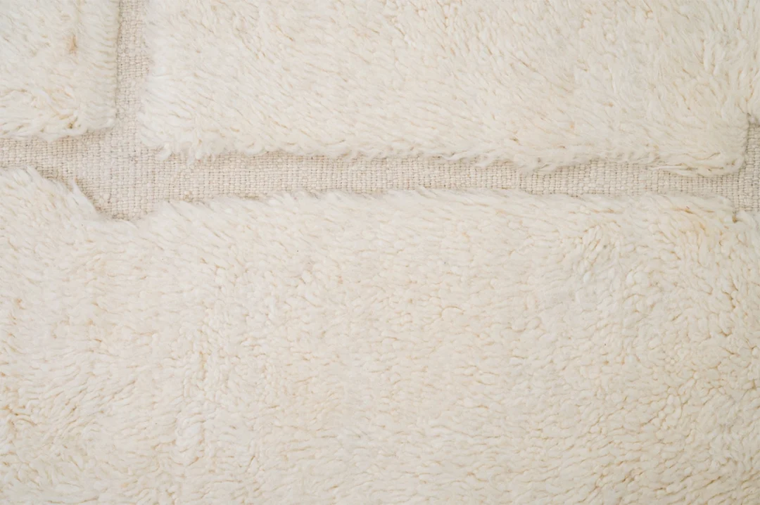 Close-up view of overlapping cream-colored, fluffy textile pieces laid out on a woven beige surface.