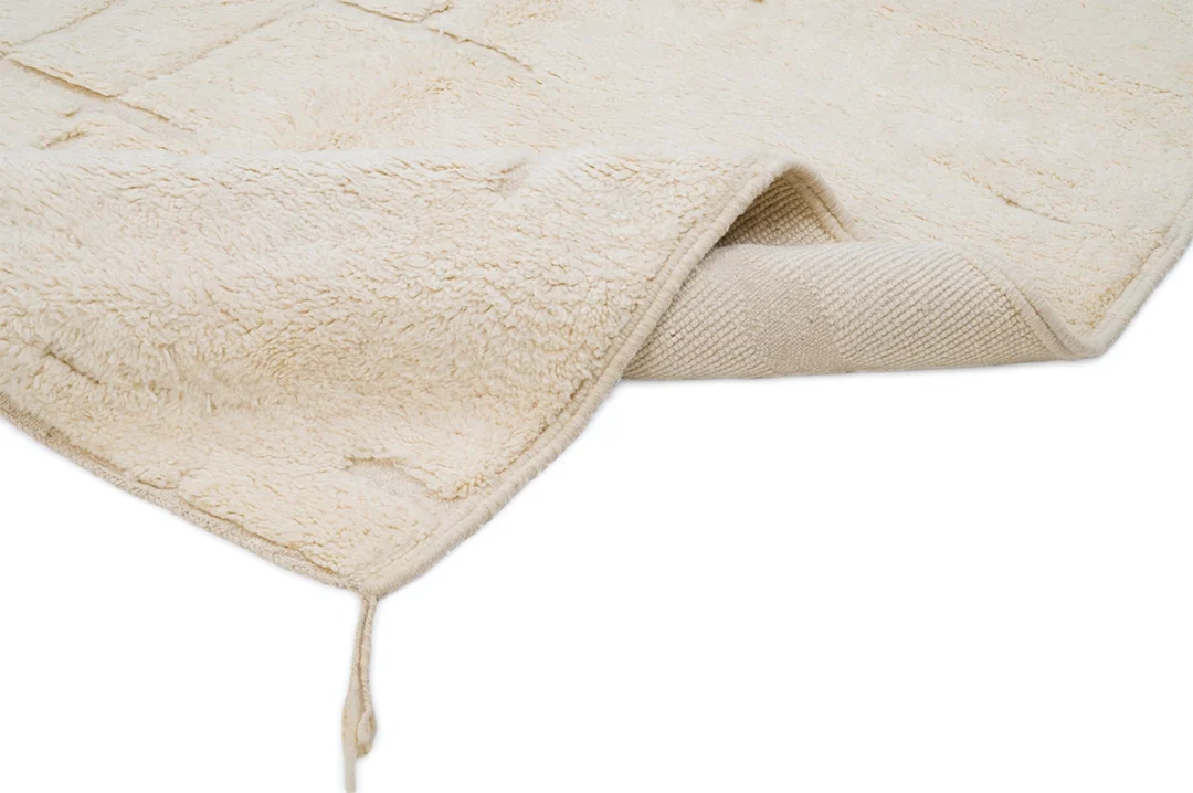 A beige, textured rug with a corner flipped over, showing the underside and a loose thread at one edge, on a white background.