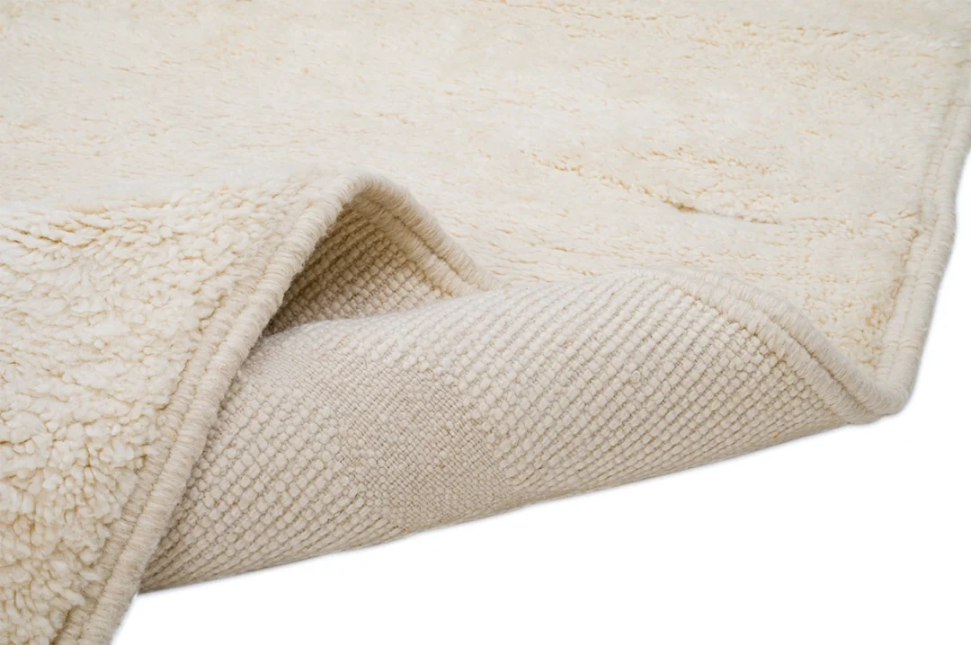 Close-up of a cream-colored textured rug with one corner folded over, showing both the soft, plush surface and the woven underside.