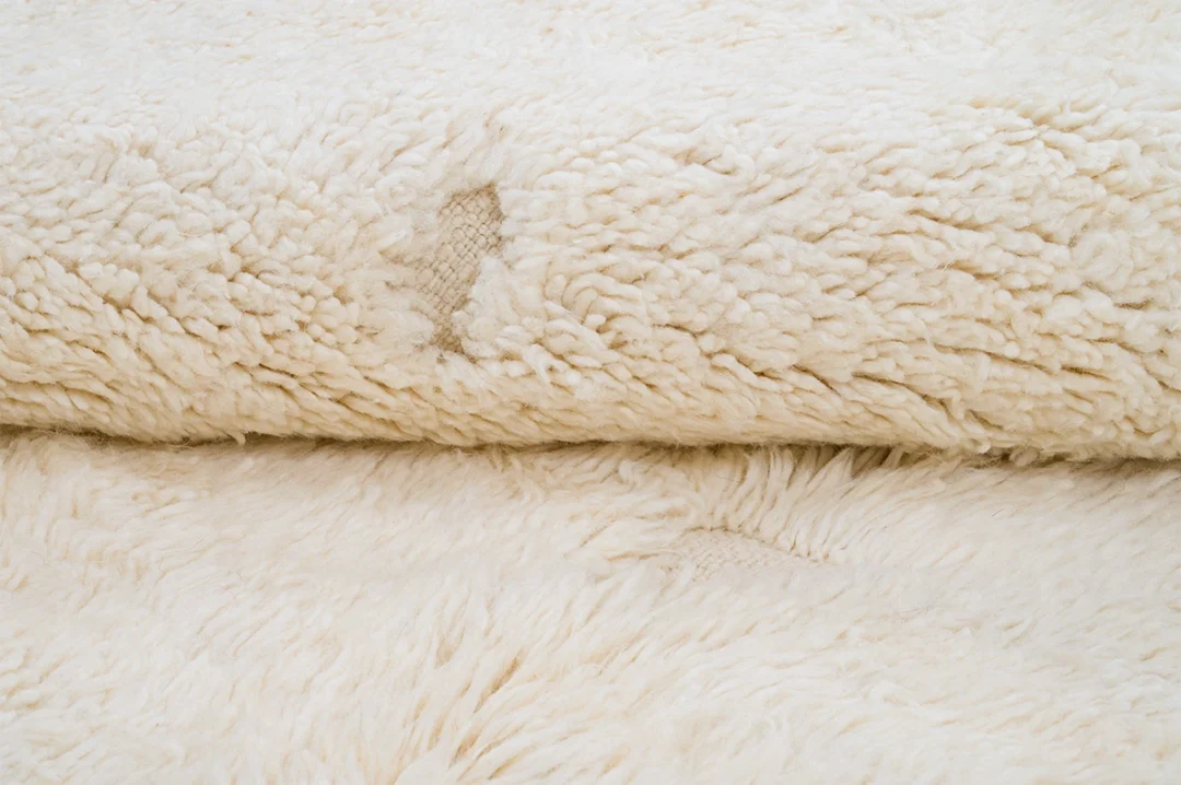 Close-up of a textured, off-white fleece fabric with some visible stains and signs of wear.