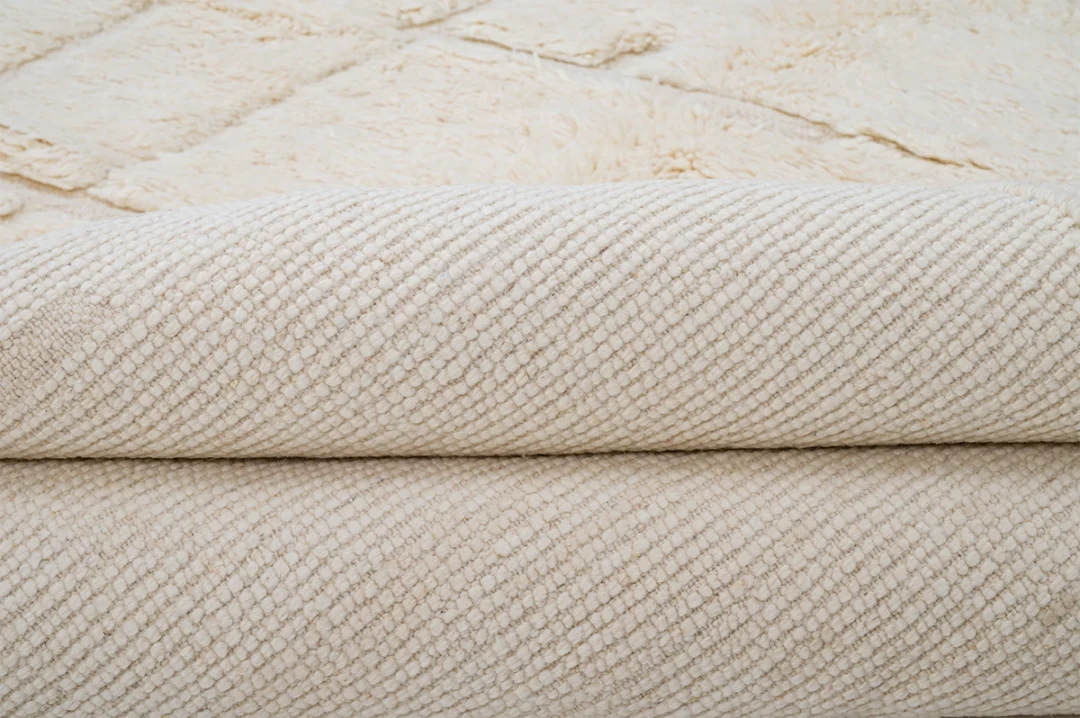 Close-up of a folded cream-colored textured rug with a diamond pattern visible in the background.