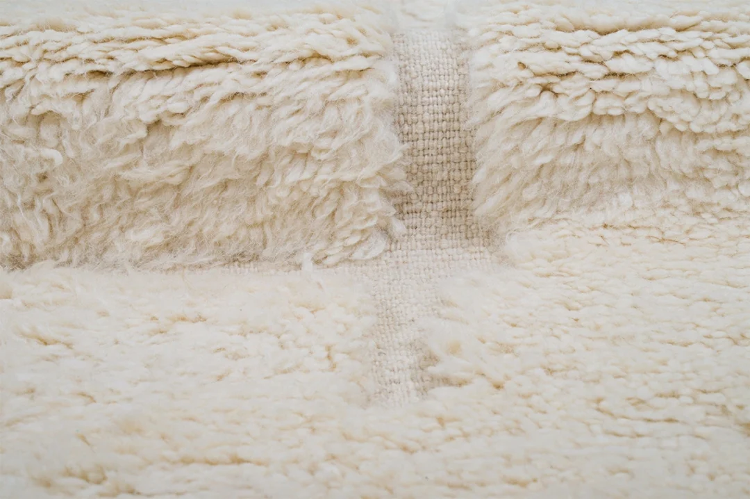 Close-up of a cream-colored, textured wool rug showing a central ridge and various pile heights.