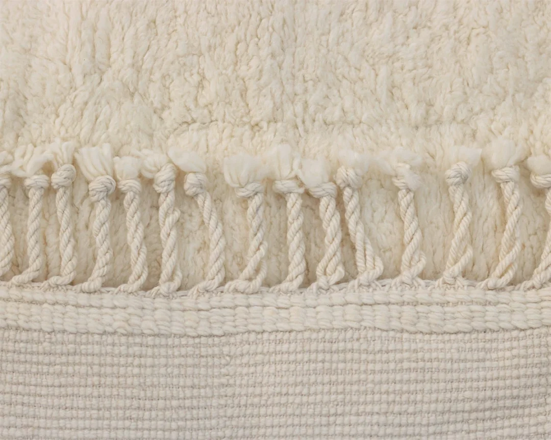 Close-up of a textured cream-colored woven rug with twisted fringe tassels along one edge.