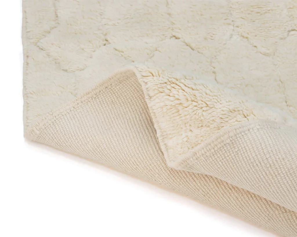 A cream-colored textured rug with one corner flipped over, revealing a woven backing and plush, patterned surface.