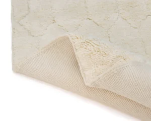 A cream-colored textured rug with one corner flipped over, revealing a woven backing and plush, patterned surface.