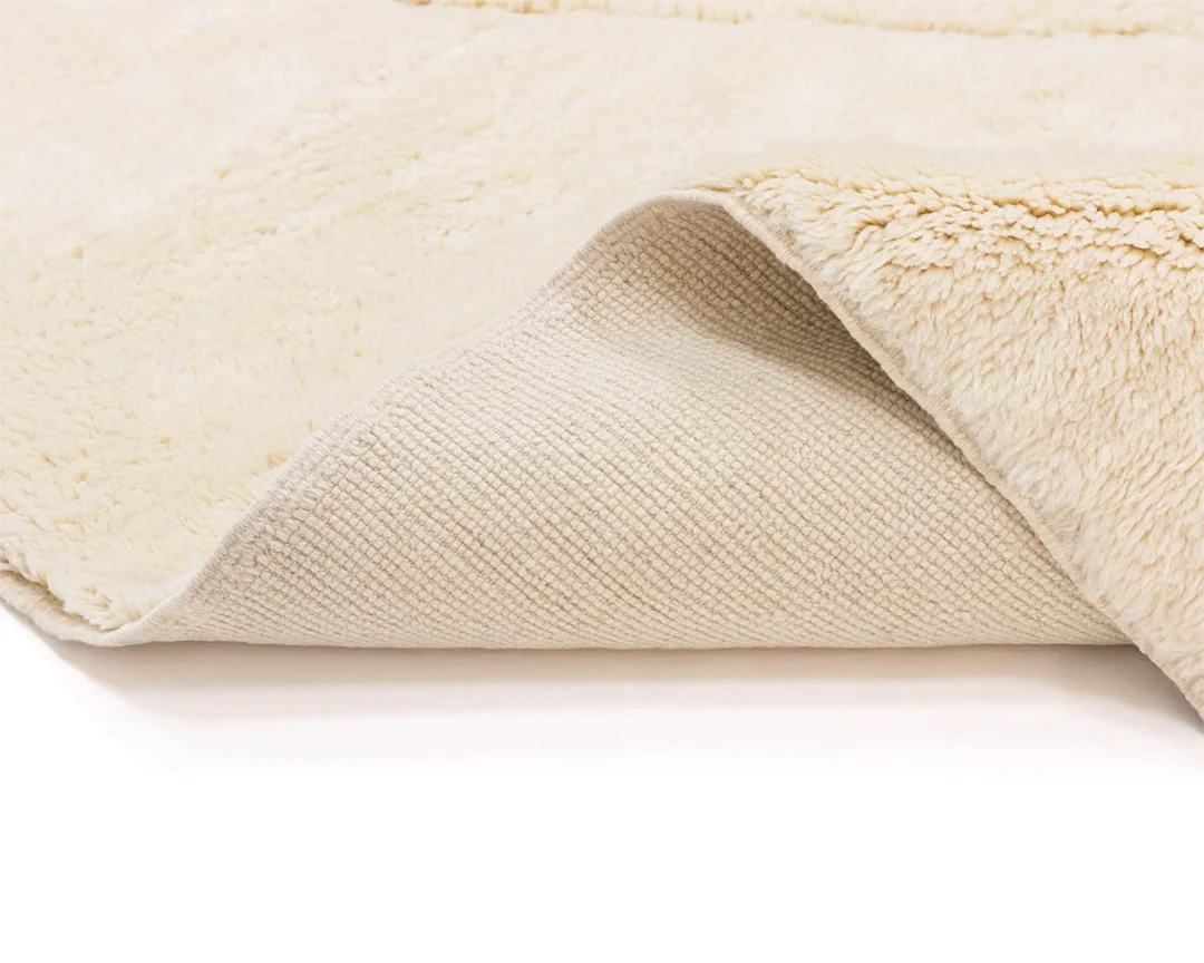 A close-up of a cream-colored, fluffy rug showing the soft, plush top layer and a textured, non-slip backing.