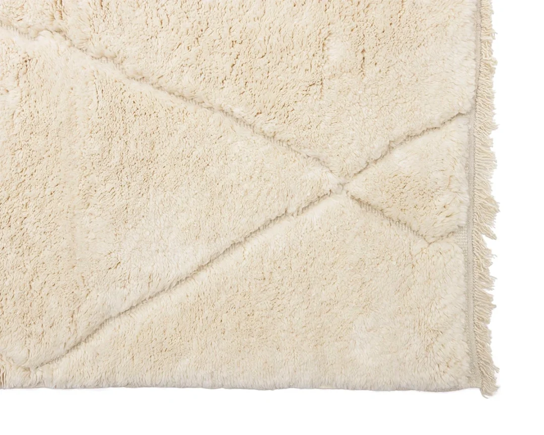 Close-up of a beige, fluffy rug with a subtle geometric pattern, showing the texture and part of the rugs border.