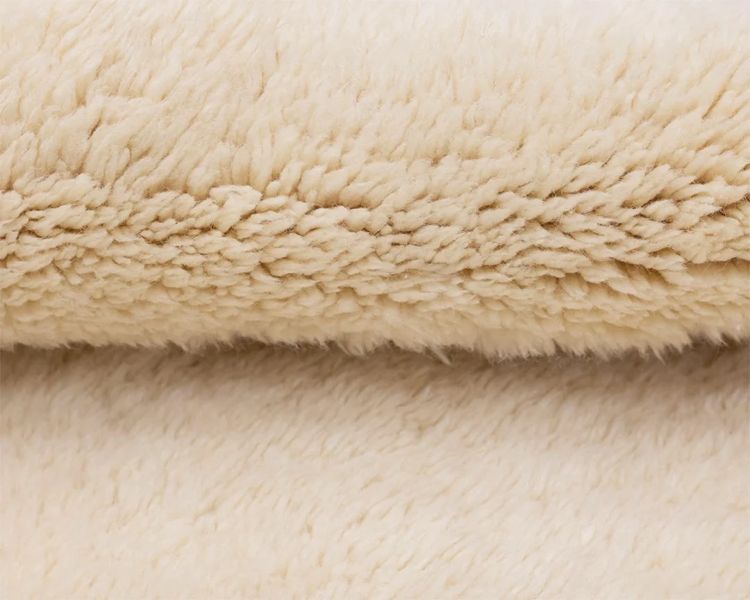 Close-up view of a soft, beige, fluffy rug with a thick, textured surface, likely resembling fleece or faux fur.
