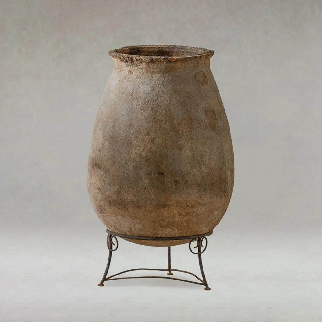 Large, weathered clay jar with a wide mouth, displayed upright on a simple metal stand against a neutral background.